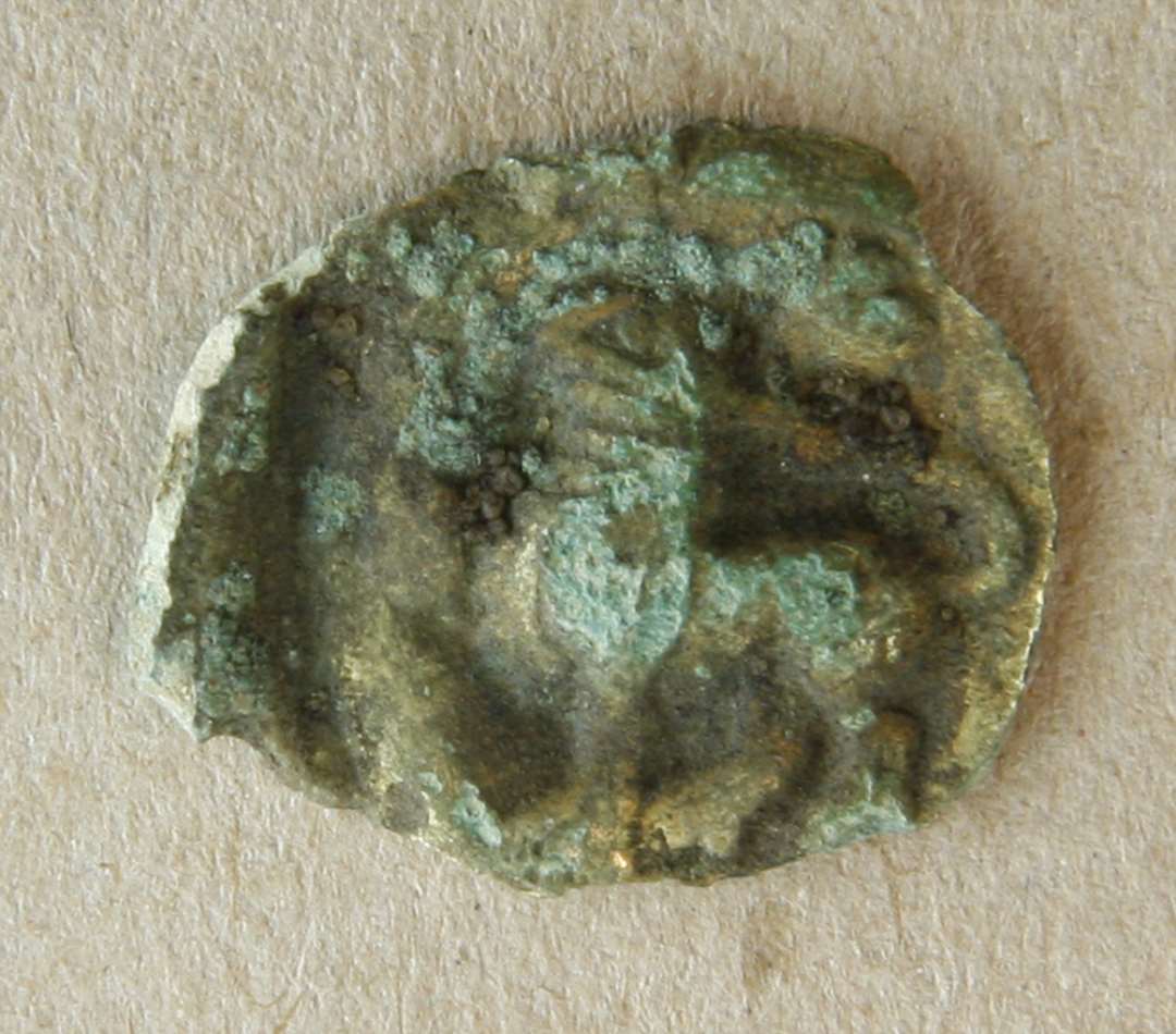Plaket af bronzeblik. Formentlig påsyningssmykke fra 12-1300-tallet, af bronzeblik med rester af forgyldning og med et stående dyr (løve?) som motiv Diameter: 21 mm.