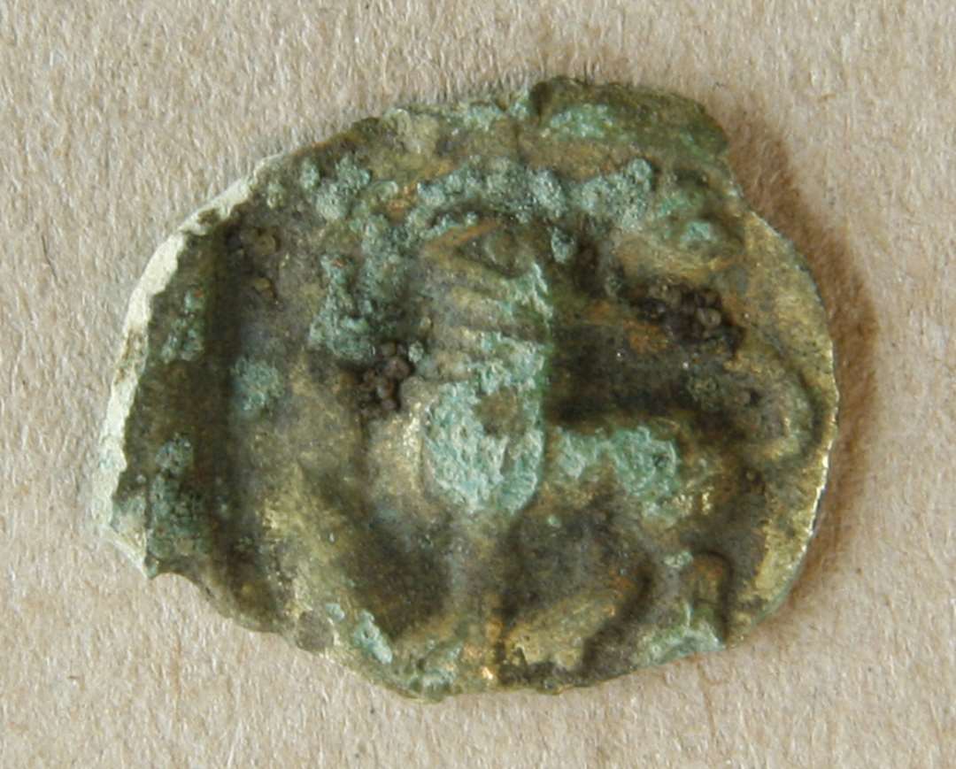 Plaket af bronzeblik. Formentlig påsyningssmykke fra 12-1300-tallet, af bronzeblik med rester af forgyldning og med et stående dyr (løve?) som motiv Diameter: 21 mm.