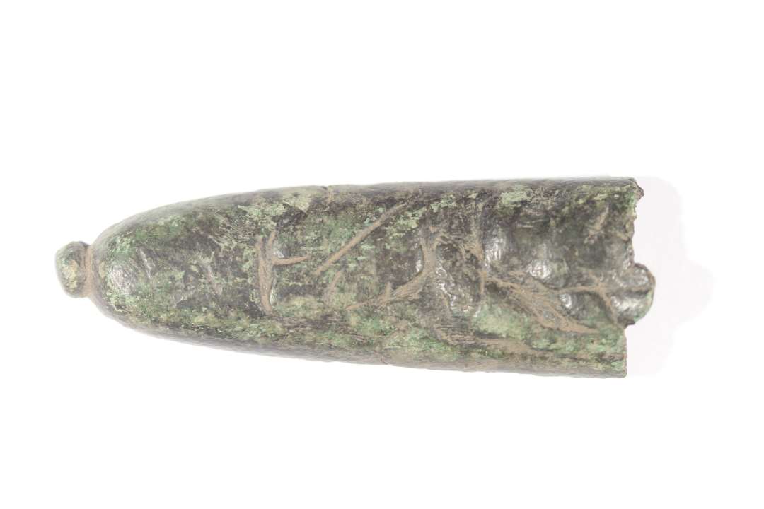 Den ene halvdel af en dupsko. Med endeknop. Ridse/hugskader eller meget grov ornamentik på overfladen. Længde: 6,5 cm., bredde: 2,2 cm.