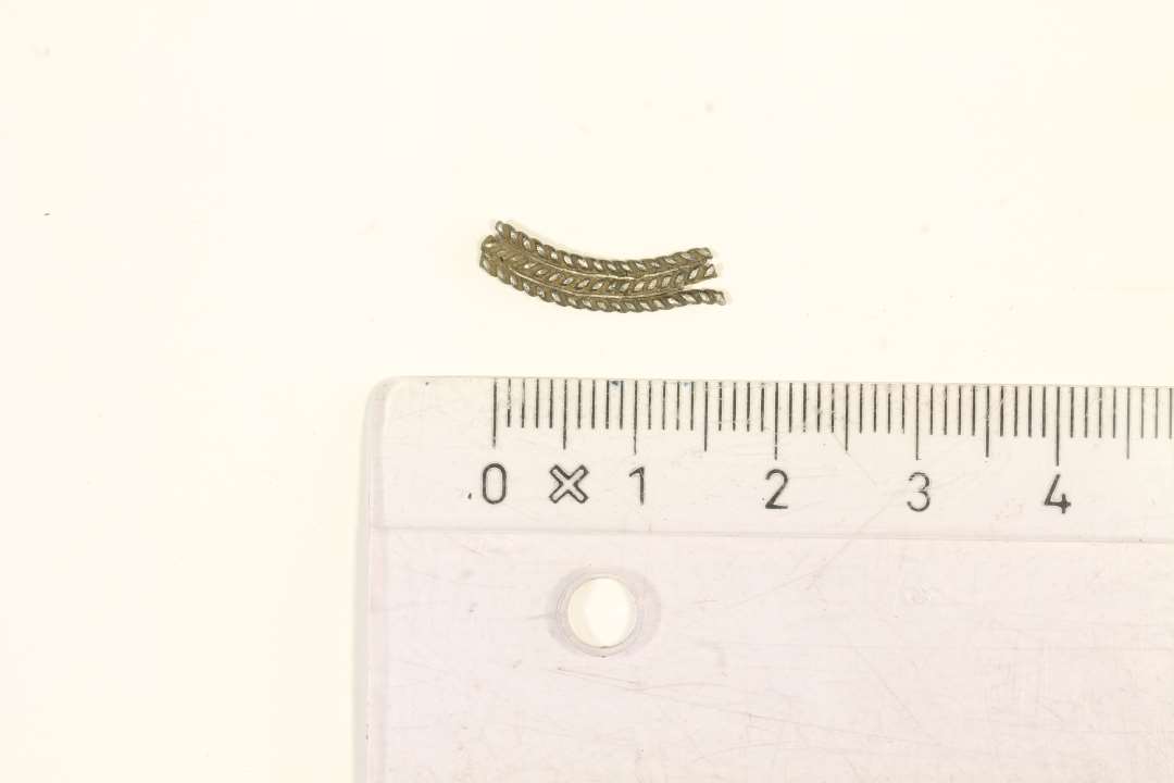 En lille stump sølv. Sammensat af tre snoede stølvtråde. Bredde: 0,3 cm., længde: 1,8 cm.