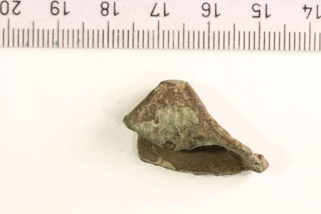 Fragment af sværdfæsteknap fra yngre germansk jernalder. Bronze med indridset ornamentik. Største mål: 3,3 cm.