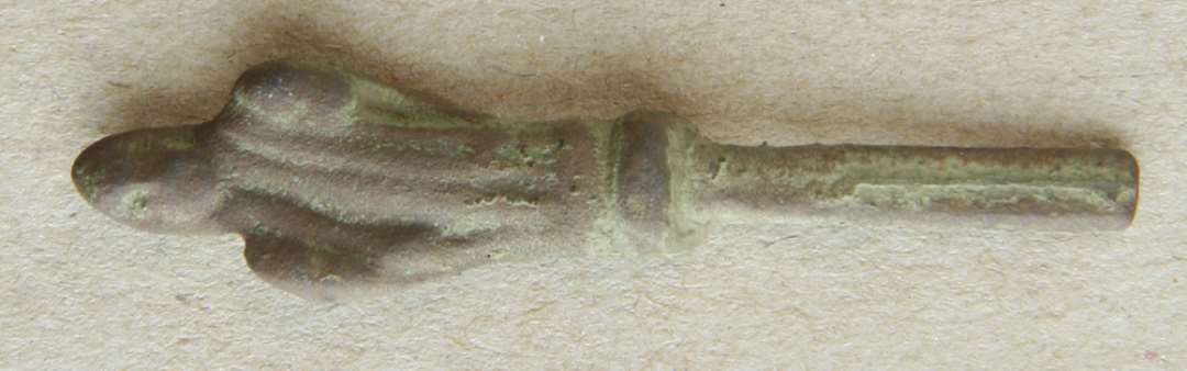 En del af skaftet og knoppen af en ske af kobberlegering. Fragmentet er ffra en såkaldt apostelske, knoppen er udformet som en menneskefigur iklædt en folderig dragt. Længde: 5 cm.