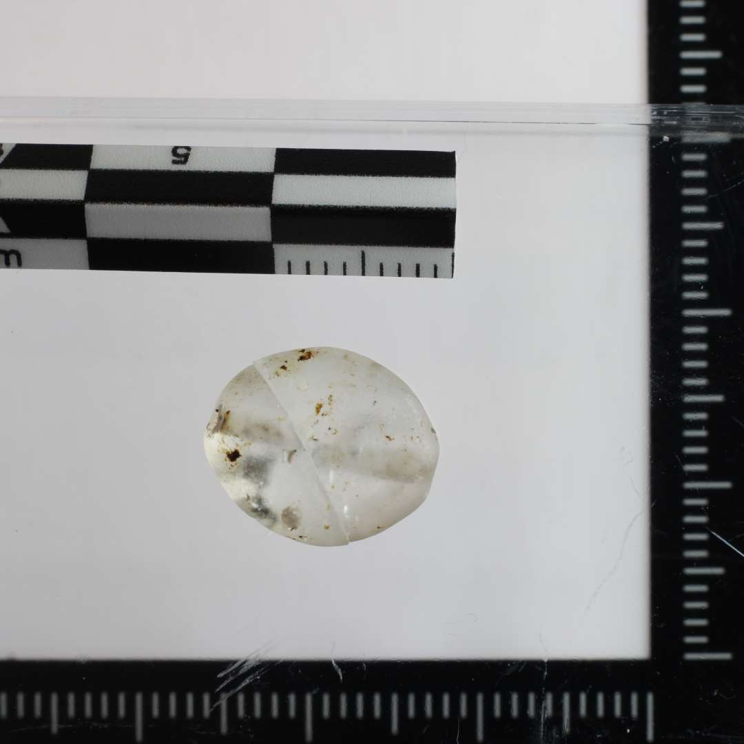 Hel perle med ovalt omrids og med spidsovalt tværsnit, hvor perlens to sider er markeret af en let ujævn, men tydelig markeret kant. Boret fra begge ender, men der mangler knap en milimeter for at hullerne når sammen.
Mat i tør tilstand, men i våd nærmest glasklar.
Ca.12x10x6 mm.