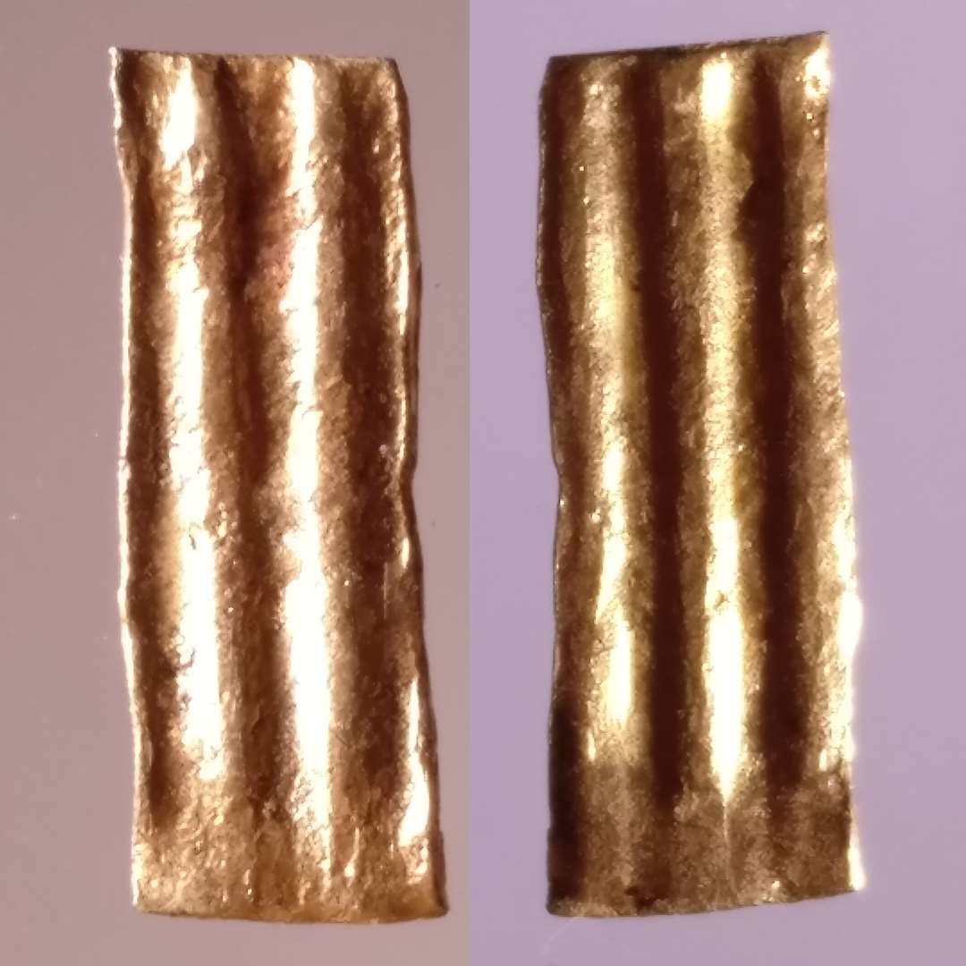 Båndformet guldstykke, 3,8 x 11 mm, med bracteatpræg (gennemgående) af parallelle furer/vulster på den lange led. Tydelig afklippet på alle fire sider, evt. komplet.