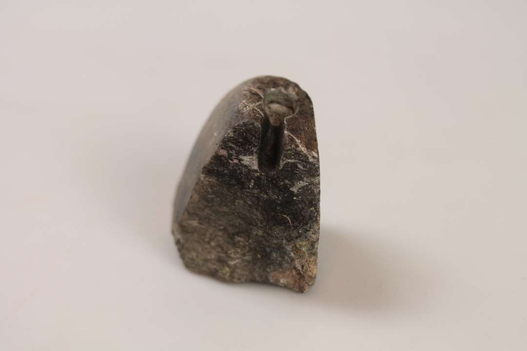 Fragment af avlsten med rilleornamentik på siden samt støbeformsudskæring til fingerformet barre der hænger sammen med cirkelformet fordybning
Mål: (5,5) x 4,5 x (5,5) cm.