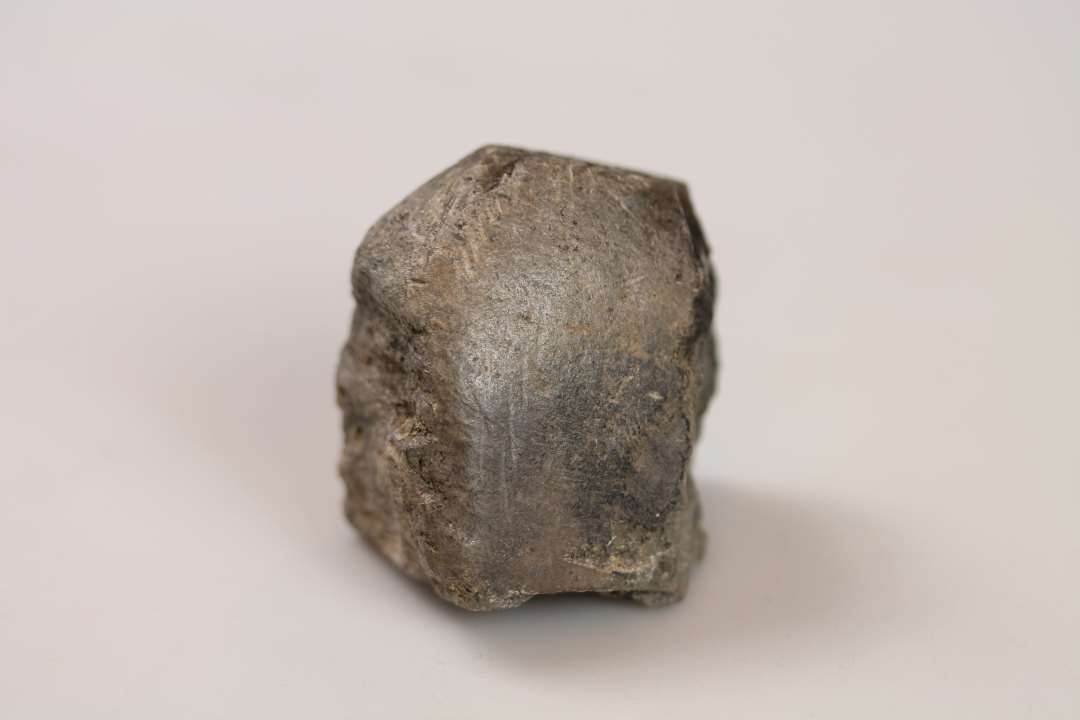 Fragment af avlsten med rilleornamentik på siden samt støbeformsudskæring til fingerformet barre der hænger sammen med cirkelformet fordybning
Mål: (5,5) x 4,5 x (5,5) cm.