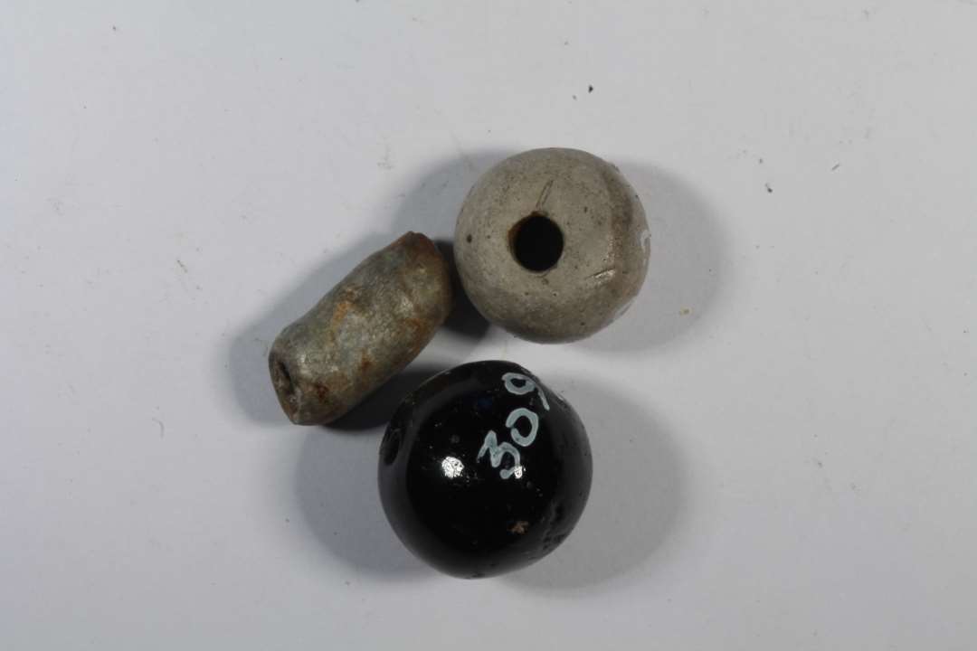 Tre perler. Én gulliggrå rørformet, én sfærisk lys grå lerperle og én med mørk brun glasur, som muligvis er fra nyere tid.  
