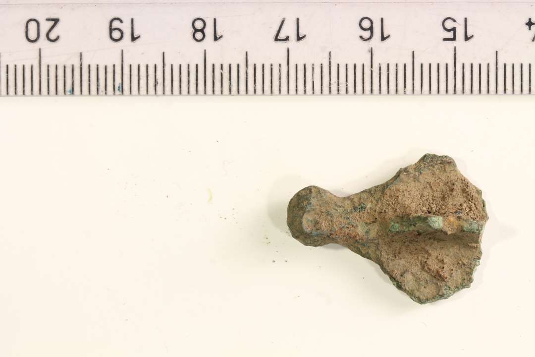 Fragment af korsformet fibel. Med profileret knop og rest af nålefæste bagpå. største mål: 2,5 cm.