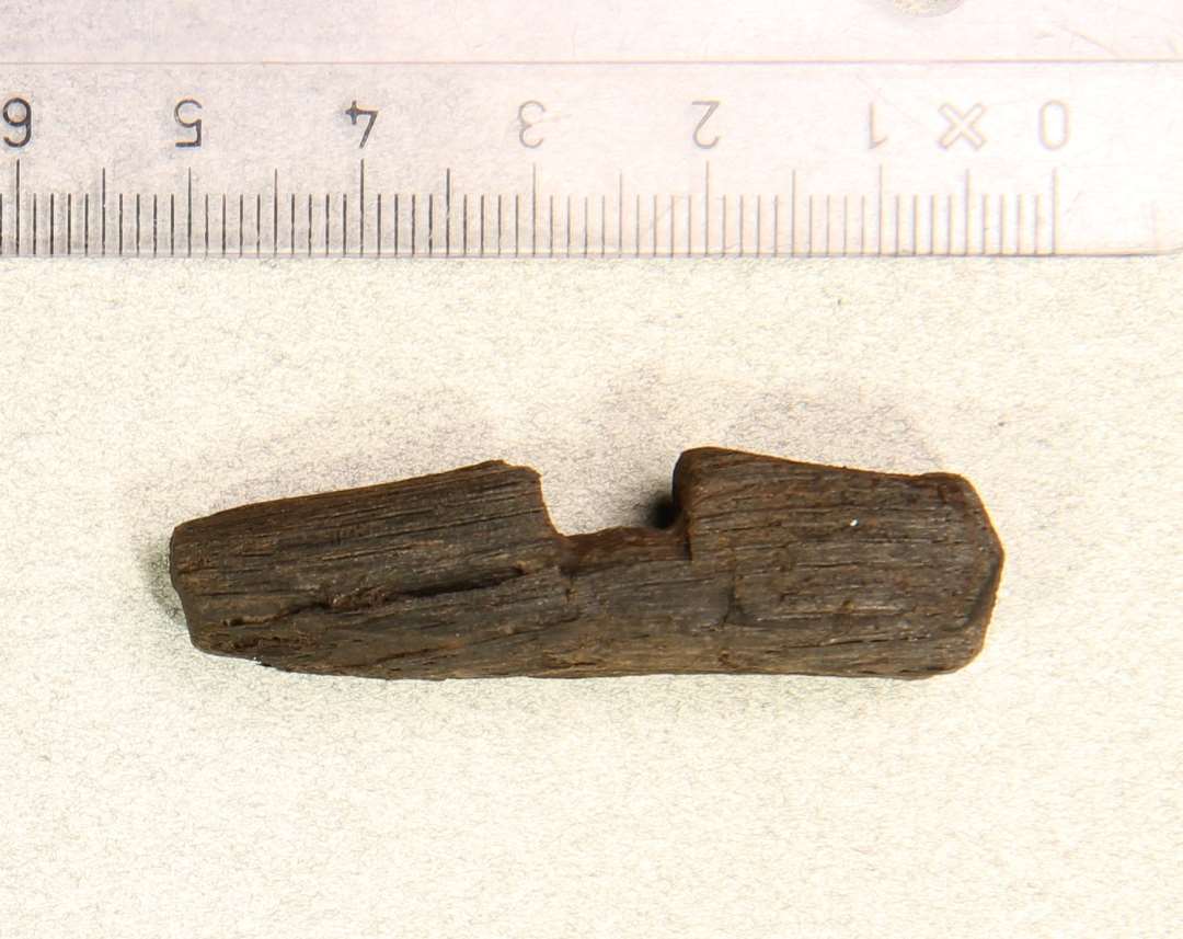 Fragment af genstand af træ. Aflang, med udsparing på midten. Længde: ca 5 cm.