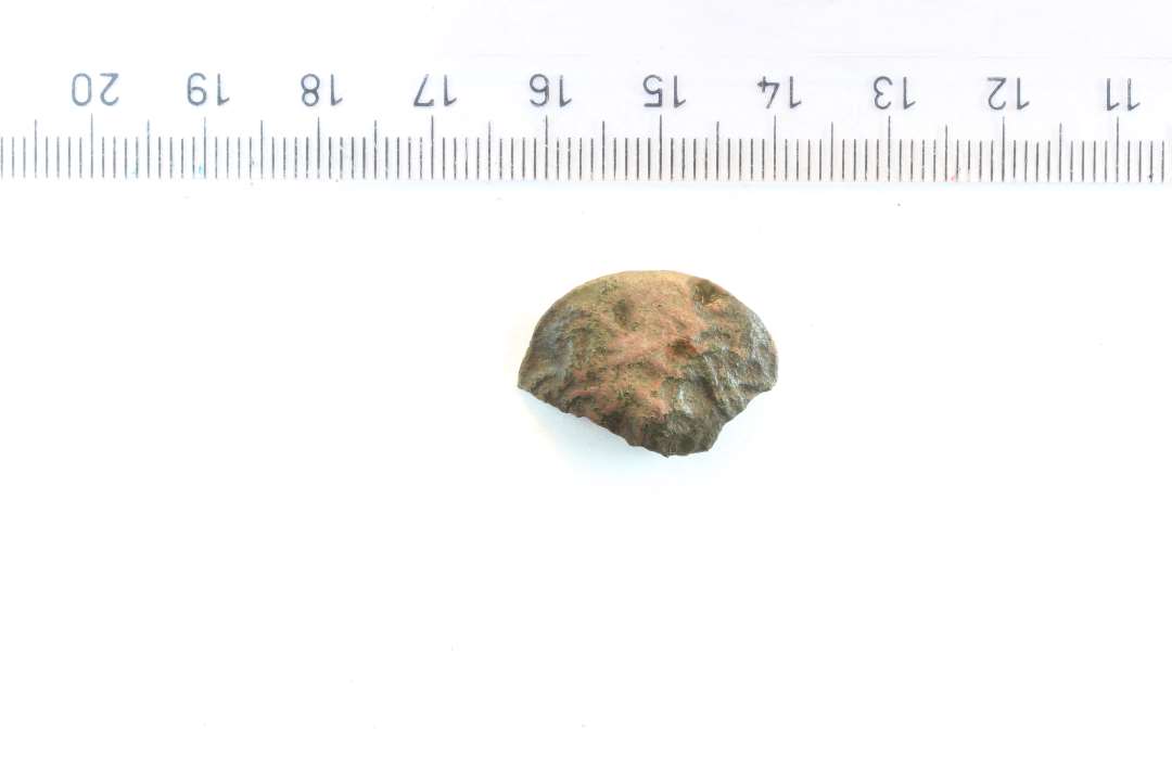 Fragment af ornamenteret skivefibel. Diameter: 2,3 cm. Rester af nålefæste på bagsiden.