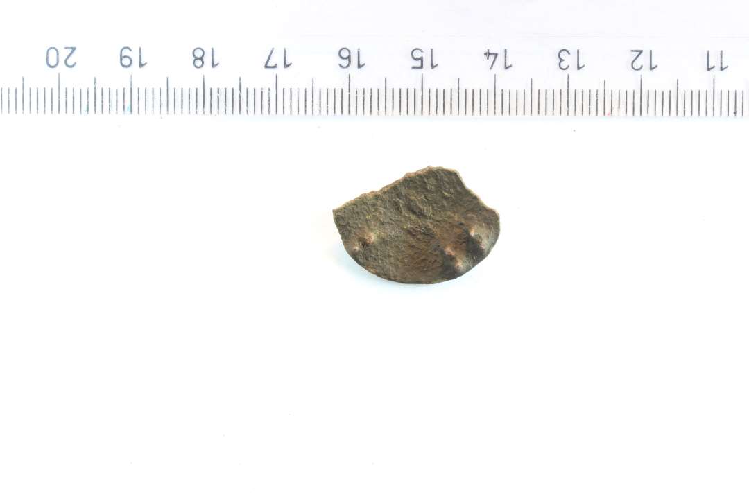 Fragment af ornamenteret skivefibel. Diameter: 2,3 cm. Rester af nålefæste på bagsiden.