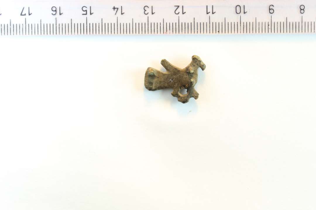 Hel lille fuglefibel, af den slags der er fremstillet i bronzestøberværkstedet i Ribe. Største mål fra næb til halespids: 1,9 cm. Fra nakketop til kløer: 1,5 cm. Med fine rester af nålefæste bagpå.