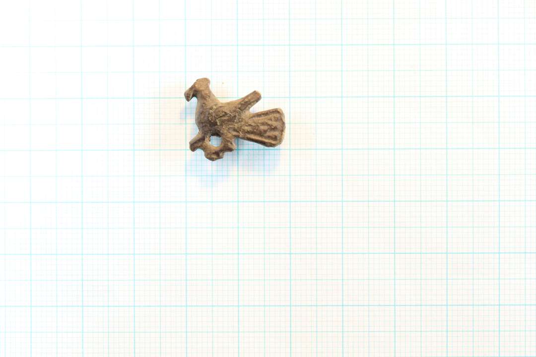 Hel lille fuglefibel, af den slags der er fremstillet i bronzestøberværkstedet i Ribe. Største mål fra næb til halespids: 1,9 cm. Fra nakketop til kløer: 1,5 cm. Med fine rester af nålefæste bagpå.