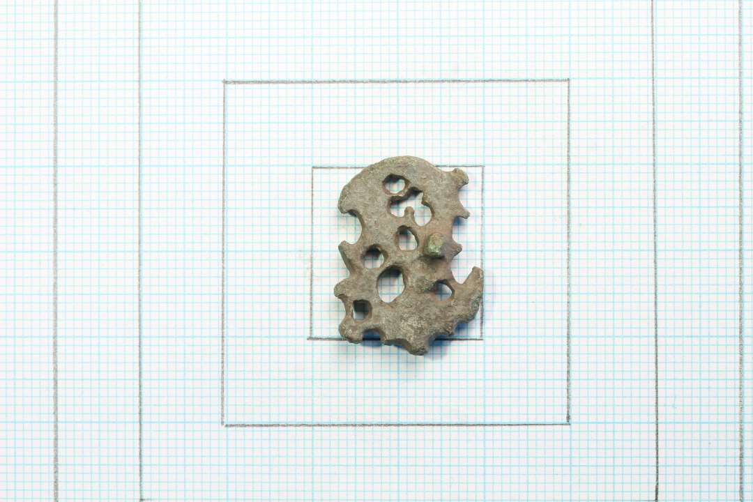 Fragment af fin urnesfibel. Nålefæsterest på bagside. Mål: 2,4x1,7 cm.